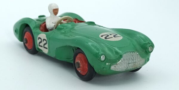 Vue de 3/4 avant d'une Aston Martin DB3S/4 de 1953reproduite par Dinky Toys GB verte avec numéros de course, son châssis est oxydé, des traces d'humidité sur la peinture rouge des roues, les numéros ont des petits manques