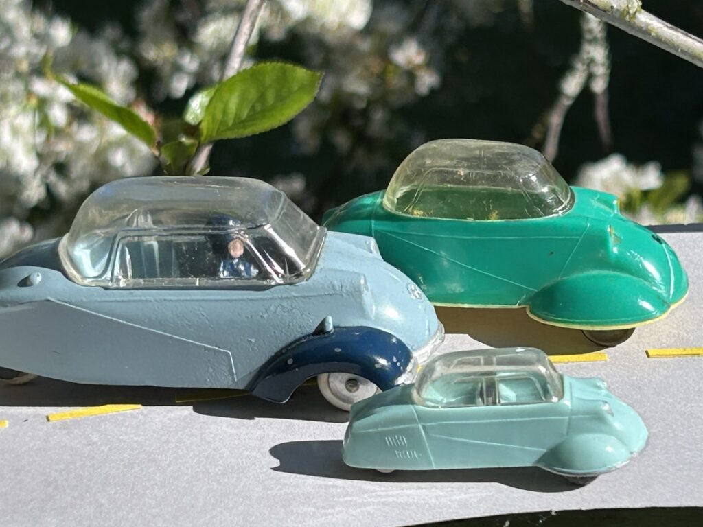 Vue plongeante de profil de trois Messerschmitt KR , 1 Siku bleu clair, 1 Quiralu bleue, 1 JUNO Plast verte, se déplaçant sur une route