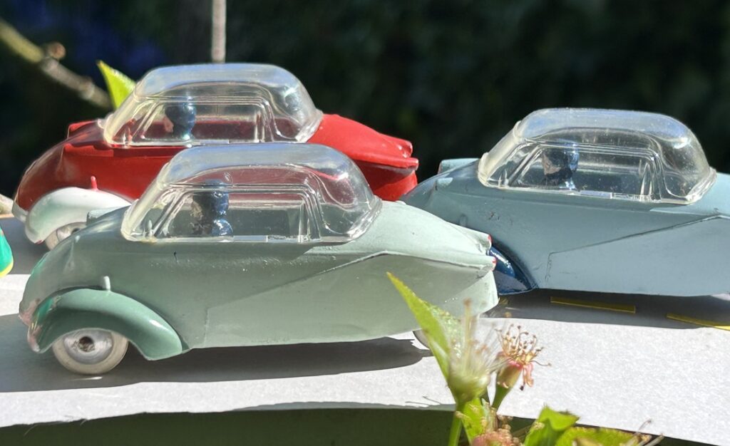 Trois Messerschmitt KR 200 Quiralu bicolores de profil négociant un virage relevé : de couleurs rouge/blanc, bleu clair/ bleu soutenu, vert d'eau/ vert gris au premier plan